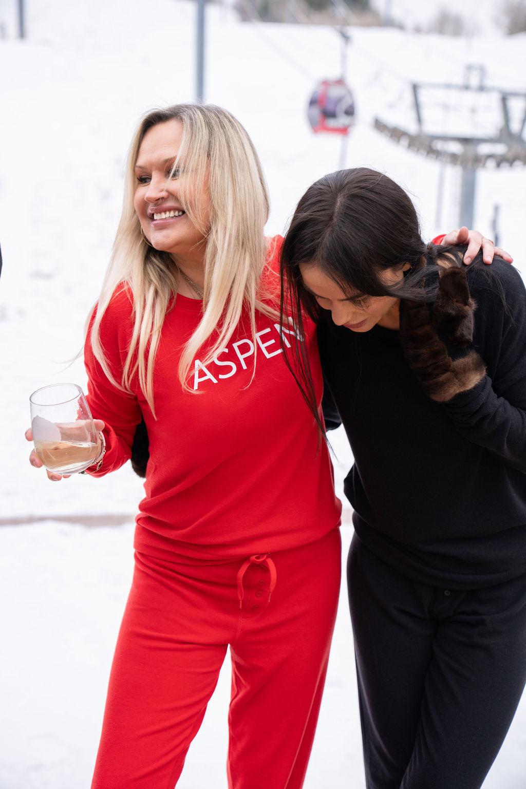 Two models wearing matching long sleeve tops in red and black, with the text 'ASPEN' printed on the front.