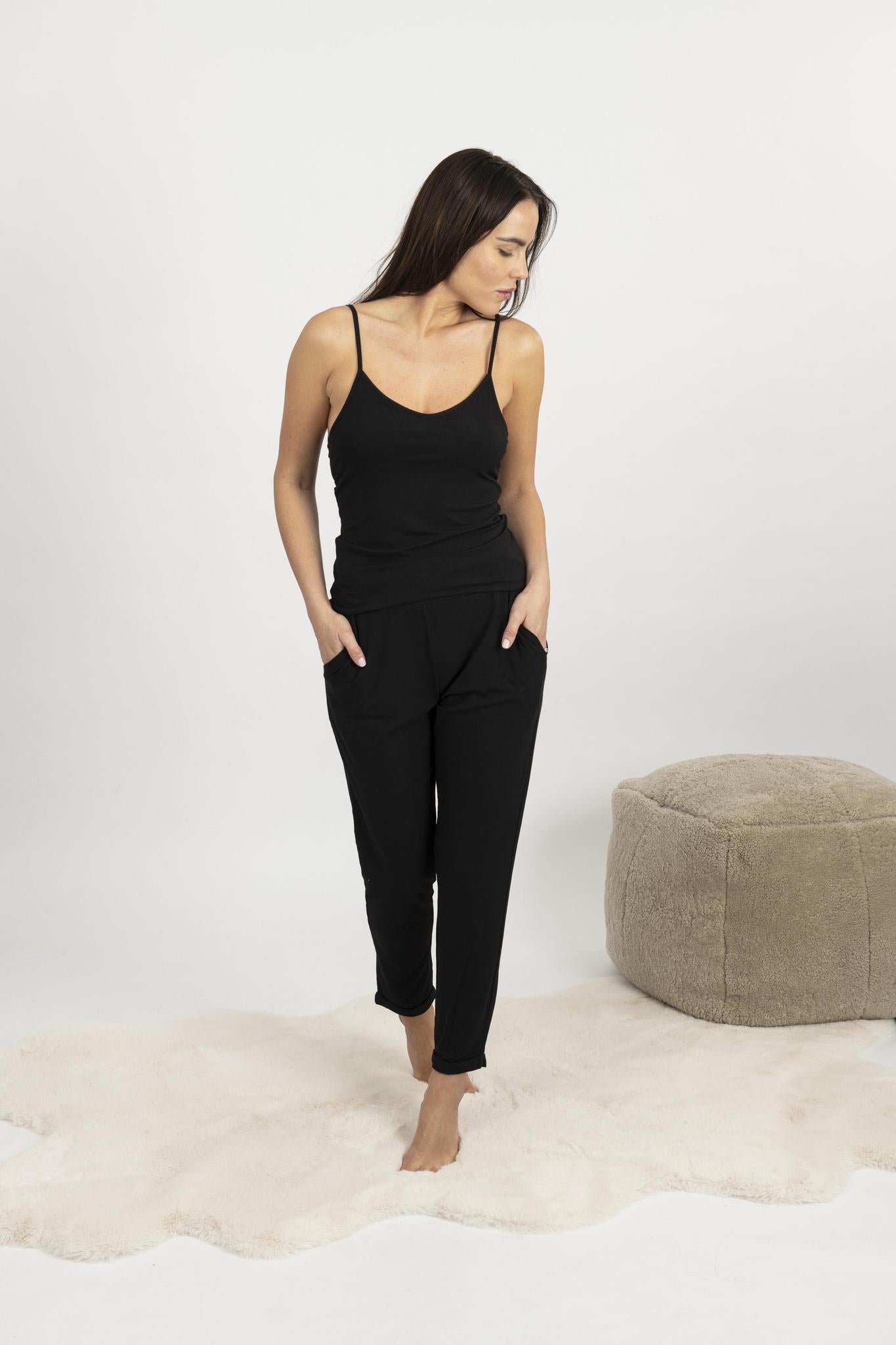 Woman wearing black ribbed cami and pants set with shelf bra and cuffed hems, lounging comfortably at home.