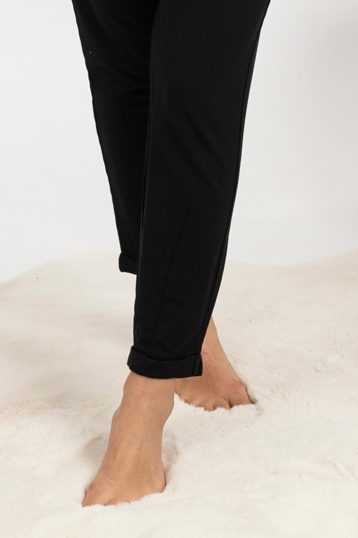 Woman wearing black ribbed pants set with shelf bra and cuffed hems, lounging comfortably at home.