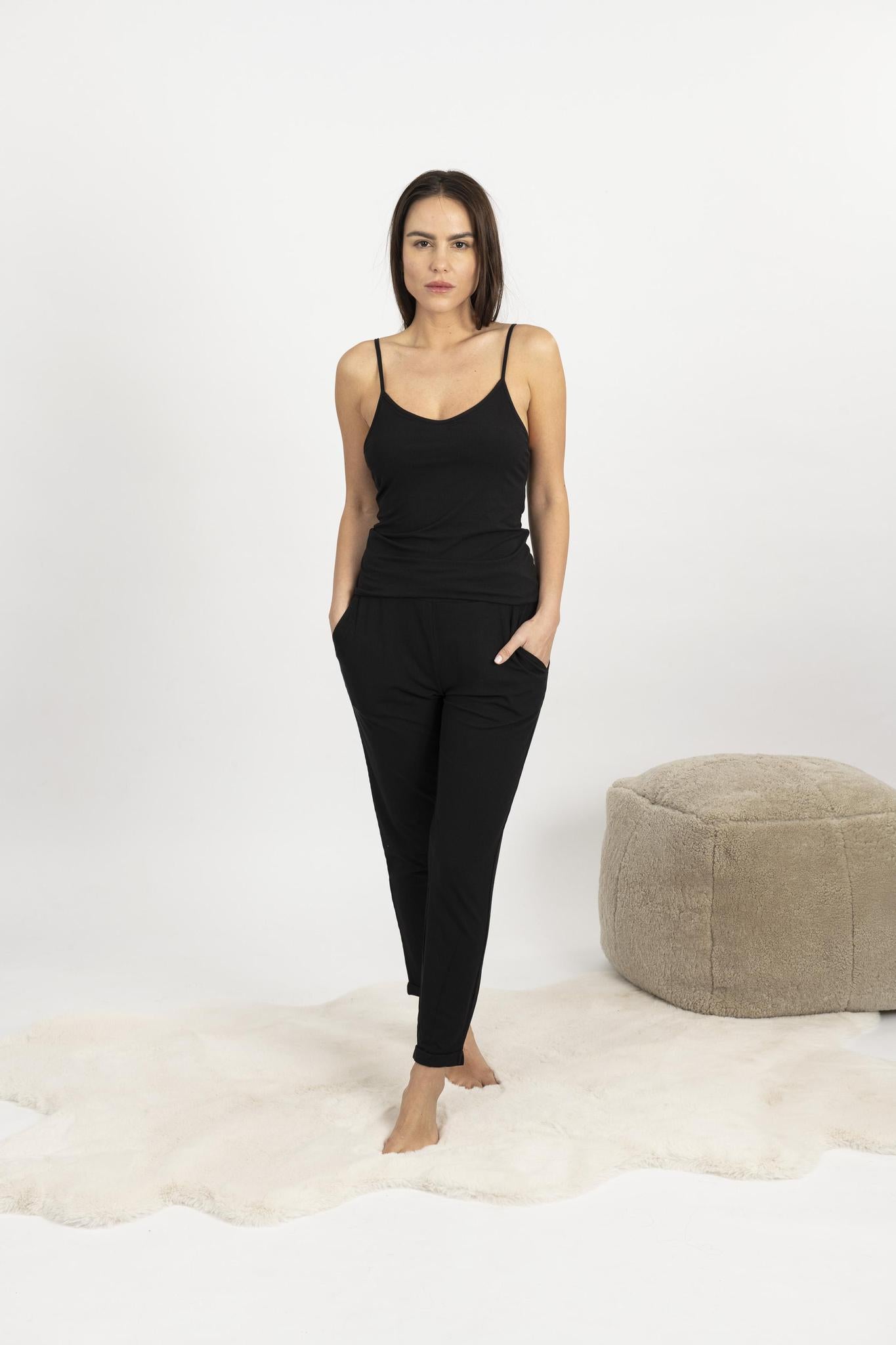 Woman wearing black ribbed cami and pants set with shelf bra and cuffed hems, lounging comfortably at home.