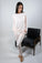 Model wearing lounge joggers in rosewater color, standing next to a black chair.